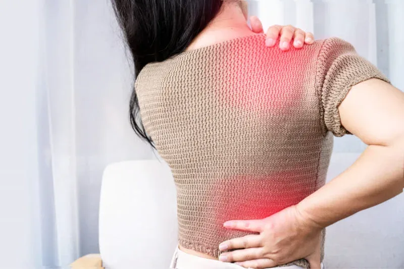 Woman experiencing fibromyalgia pain in neck, shoulder and lower back areas highlighted in red, showing widespread muscle pain that sauna therapy can help relieve