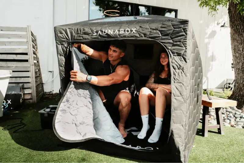 Couple enjoying steam therapy session inside SaunaBox GO two-person portable sauna tent in backyard