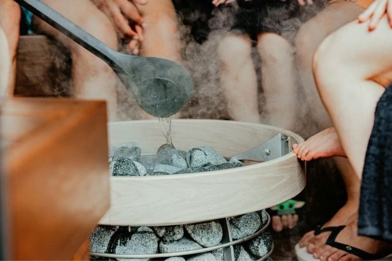 Pouring water over sauna stones with a ladle, generating steam in a traditional sauna session