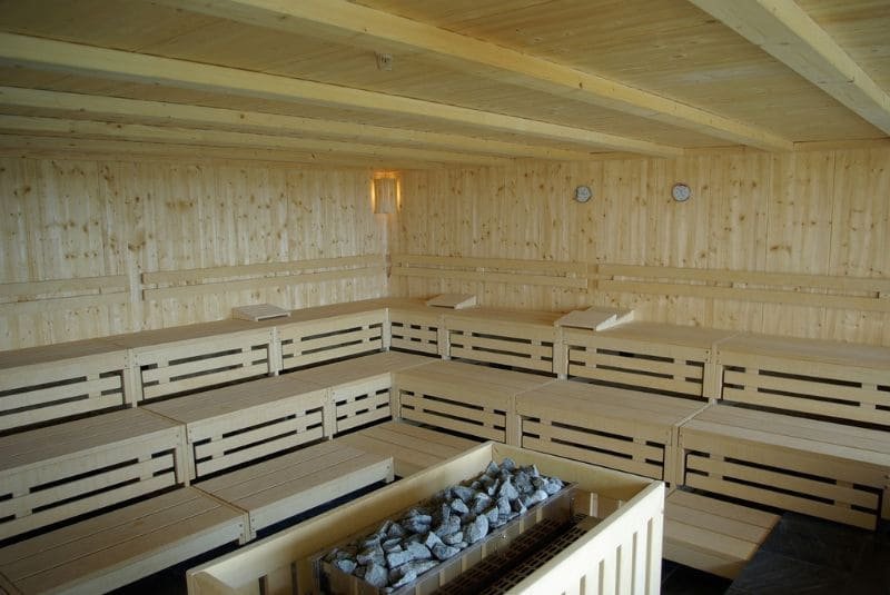 Inside view of a traditional Finnish public sauna with wooden benches and walls, and heated stones in the center