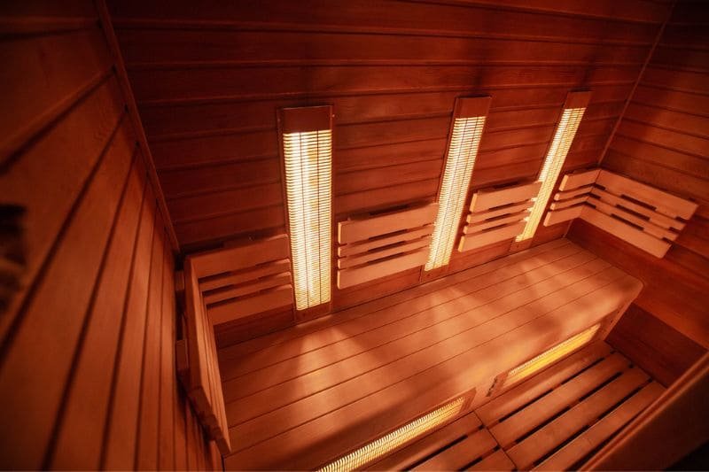 A serene infrared sauna interior with glowing heaters and smooth wooden benches, designed for peak thermal comfort and relaxation without reaching extreme temperatures.