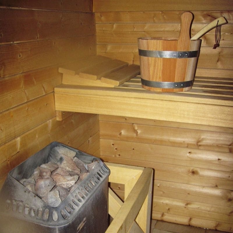A close-up view of a sauna's interior showcasing a wooden bucket with a ladle and a stove filled with hot stones, indicative of the warmth and steam generation essential for a relaxing sauna experience