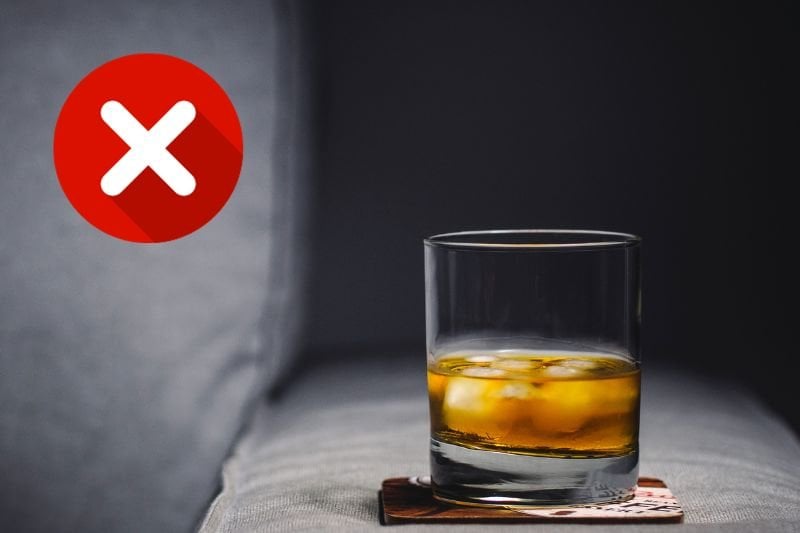 A glass of whiskey with ice marked with a red 'X', indicating to avoid alcohol before or after sauna sessions to minimize the risk of dehydration