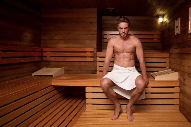 Man resting in a sauna room, experiencing the therapeutic heat and recovery post physical training.