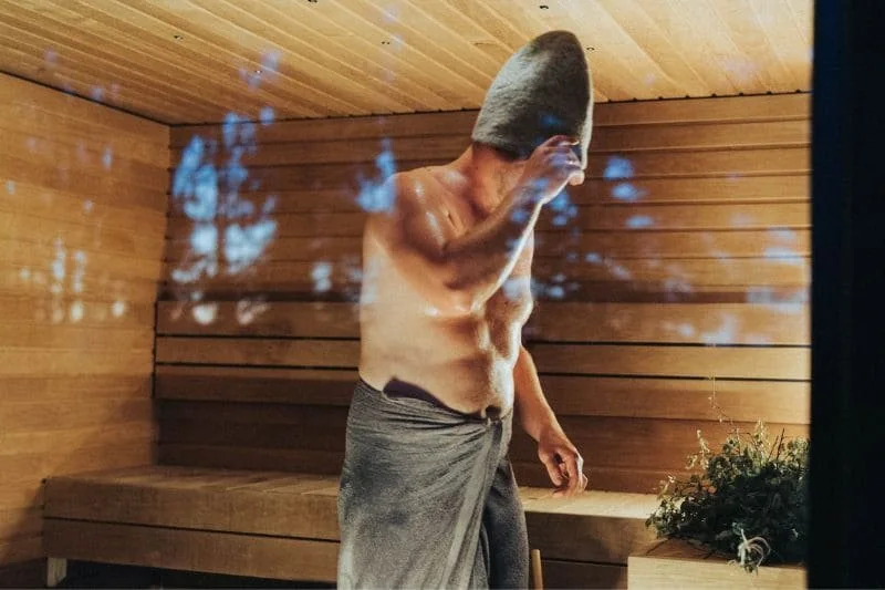 Man wiping sweat with a towel in a sauna cabin, potentially burning calories in a sauna