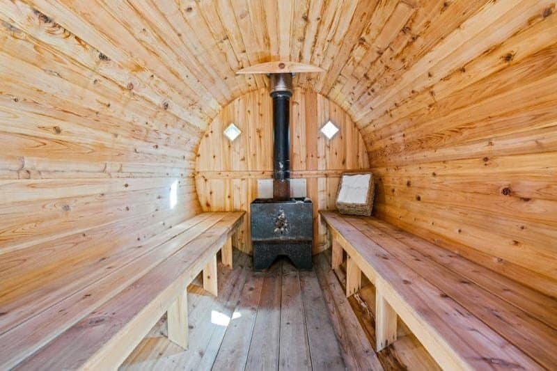 Inside view of a barrel-shaped wooden sauna with a wood-burning stove, highlighting rustic heat therapy ambiance.