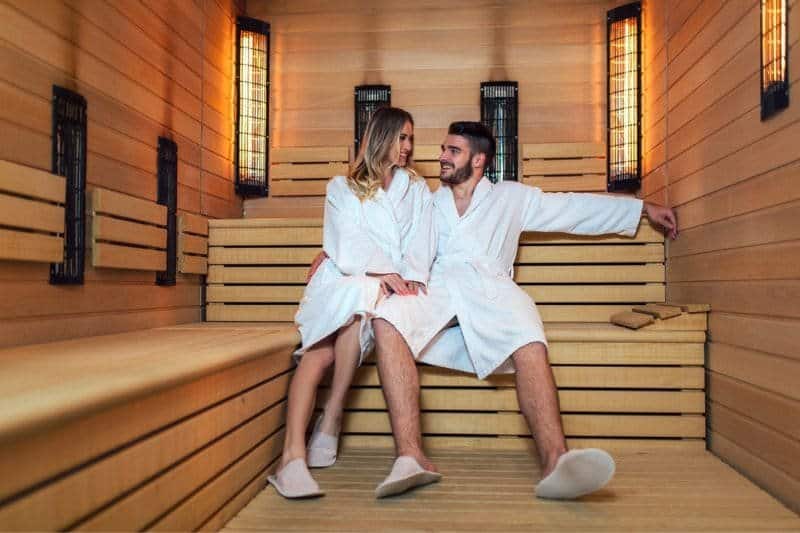 A couple enjoying a relaxing moment in a wooden sauna, reflecting on the connection between regular sauna and longevity