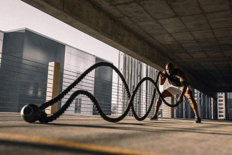 Fitness enthusiast engaged in high-intensity battle rope workout under a bridge, embodying strength and endurance in a modern urban setting.