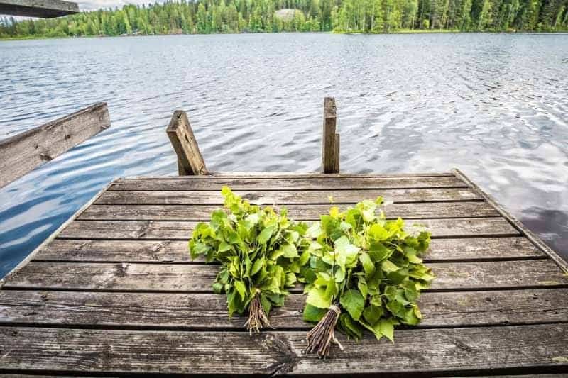 Freshly prepared sauna bundles laid out on a wooden dock by the lake, signifying the authentic sauna practice of whisking.