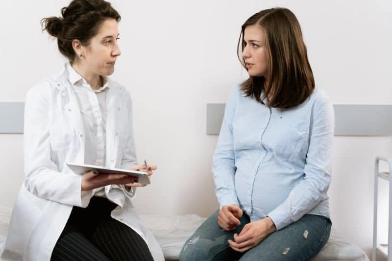 A pregnant woman discussing with a healthcare professional the safety of using an infrared sauna during pregnancy, highlighting the importance of medical advice.