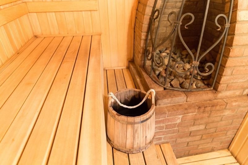 A wooden bucket beside a classic brick sauna stove, showcasing essential accessories for a steam sauna experience.