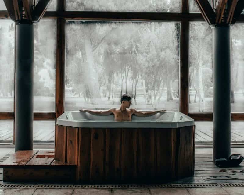A person unwinding in a wooden hot tub, surrounded by a tranquil, snow-covered landscape, showcasing a blend of warmth and winter.