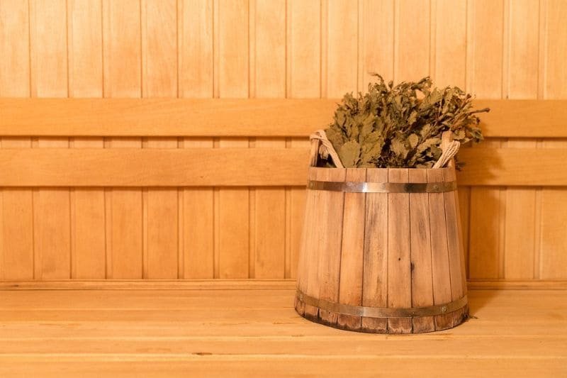 Wooden bucket holding a traditional bundle of sauna birch leaves, ready for a soothing sauna whisking ritual.