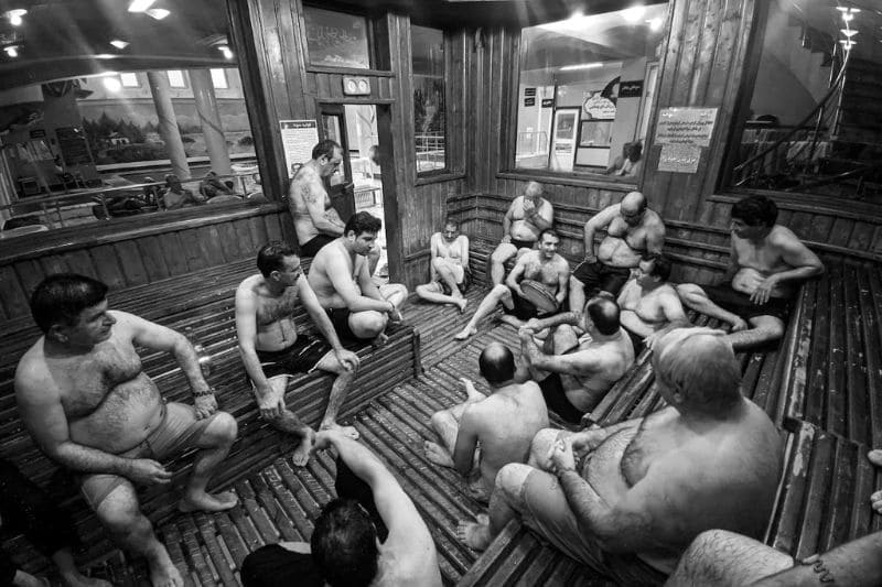 Individuals in a communal sauna respectfully sharing space, engaging in relaxed, quiet conversation while maintaining personal space.