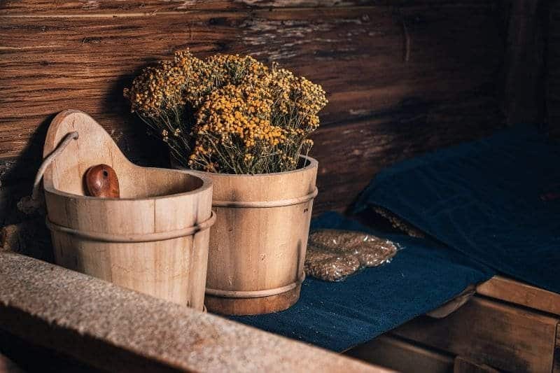 Wooden sauna accessories including buckets and ladle with dried flower sauna whisks on the bench.