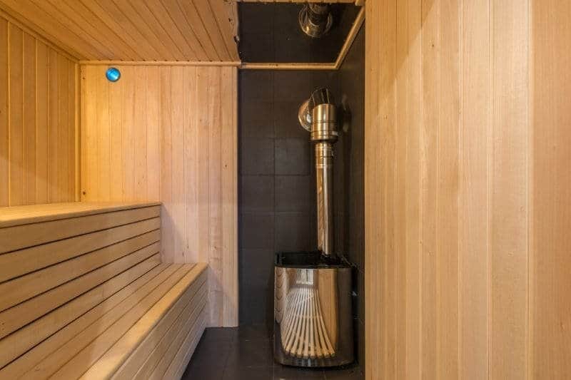 Corner view of a sauna room showing a modern heater with sauna stones.