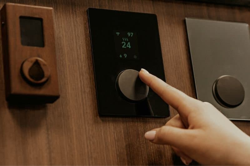 Alt Text: A hand adjusting a sauna's thermostat, a part of etiquette to consult with other users before making temperature changes in a shared space.