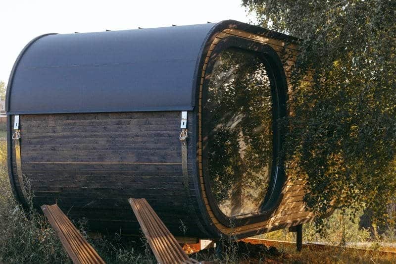 A wooden barrel sauna with a large glass door nestled among trees.