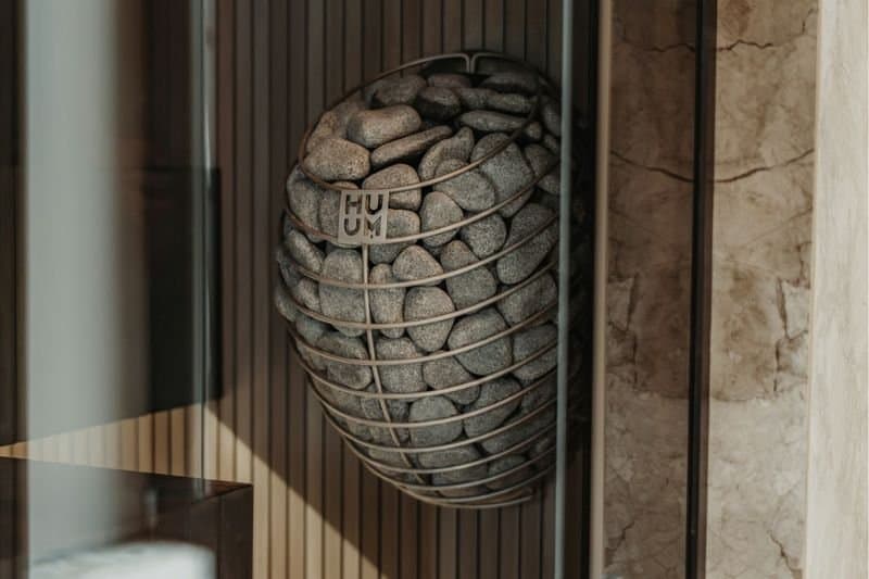 Close-up view of a round sauna heater filled with volcanic stones with the word "HUUM" inscribed on a metal plate.