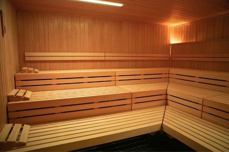 Interior of a sauna showing tiered wooden bench seating and warm lighting.