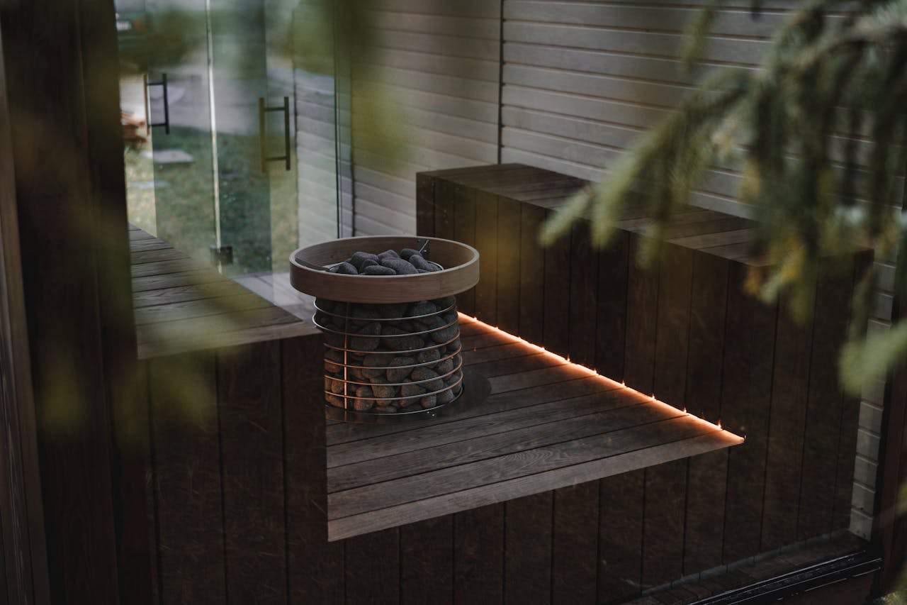 Modern wood-burning sauna heater encased in a safety grid, placed in a serene outdoor sauna setting.