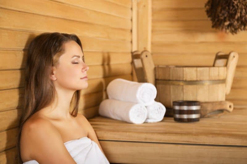Woman relaxing peacefully in a sauna with towels, wooden bucket, and whisk
