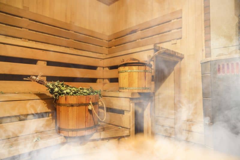Sauna interior with traditional wooden buckets and a bunch of dried branches, ready for a detoxifying sauna ritual.
