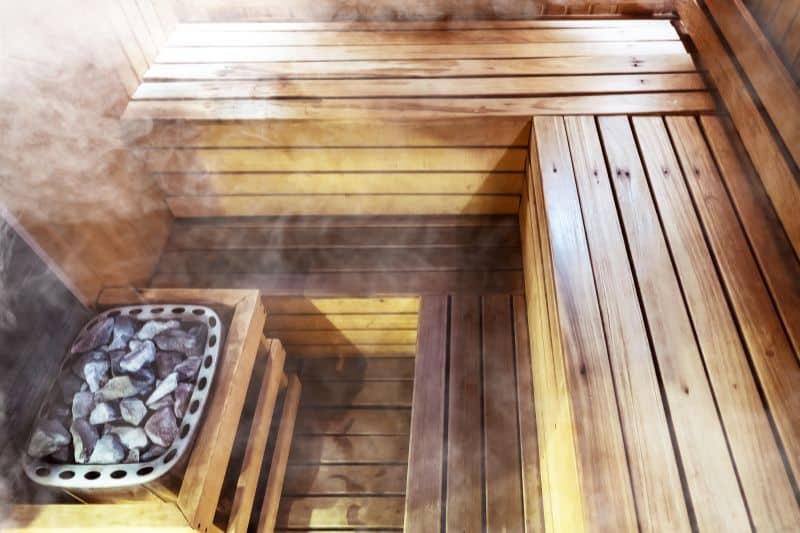Steam rising over sauna heater filled with volcanic rocks in a private sauna room.