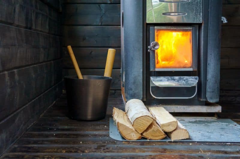 Wood-burning sauna stove with metal bucket and ladle, and wood logs ready for heating.