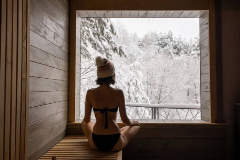 A tranquil scene of a woman in a sauna with a view of a snowy winter landscape.