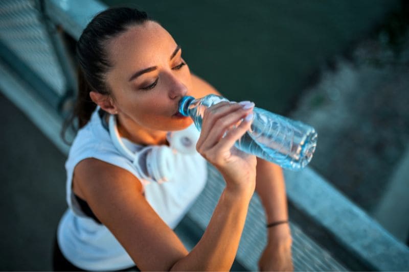 A woman hydrating with a bottle of water before going to the sauna, underlining the importance of staying hydrated especially before and after sauna sessions.