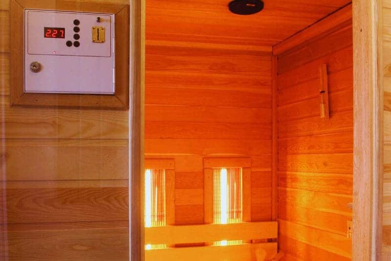 Inside view of an infrared sauna with a visible temperature control panel on the exterior side wall.
