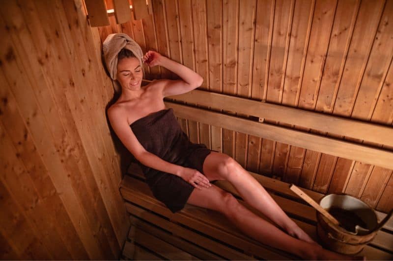 Woman enjoying a calming sauna relaxation therapy session, complete with towel wrap and ambient wooden surroundings.