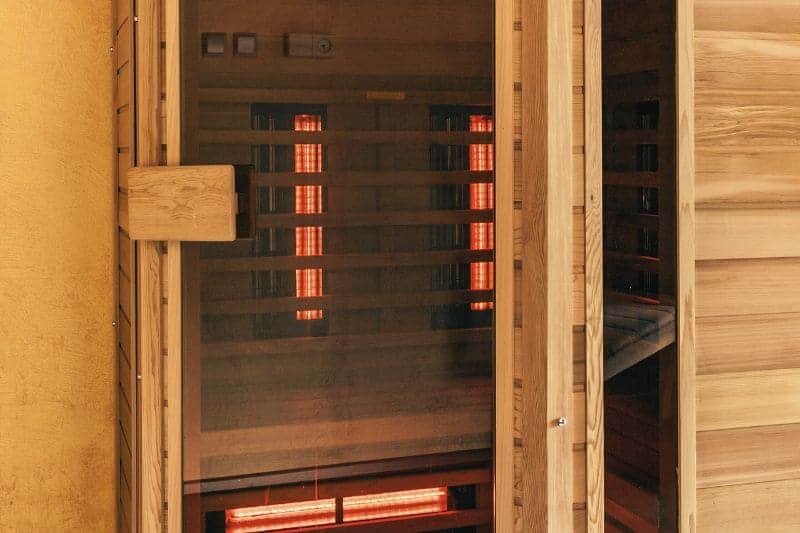 An empty and small infrared sauna with red light emanating from the infrared light panels.