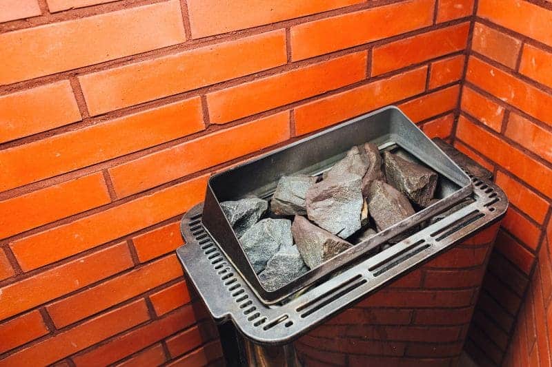 Close-up of a electric sauna heater with rocks inside a sauna with red colored bricks on the wall.