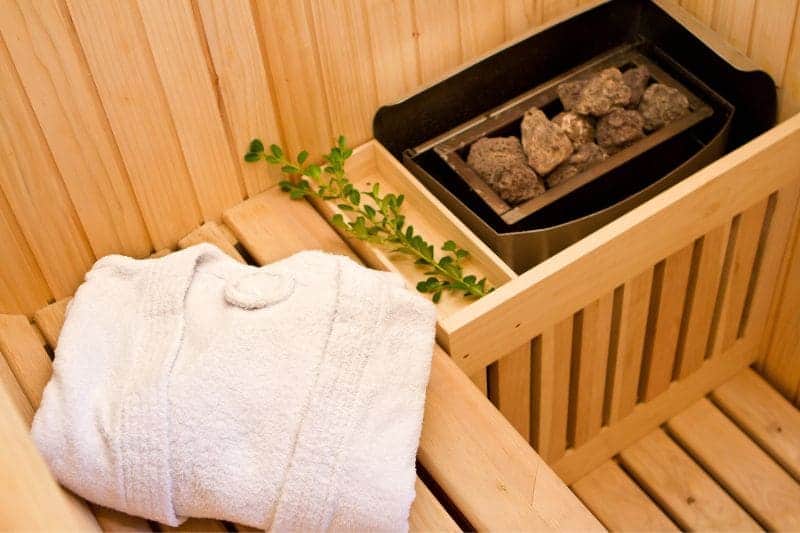Electric sauna heater with a bathrobe and a small plant stem with green leaves, inside a sauna, illustrating a modern and convenient sauna experience.