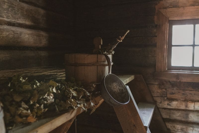Traditional sauna accessories including a wooden bucket, ladle, and vihta on a bench inside a rustic sauna, evoking a sense of warmth and tranquility.