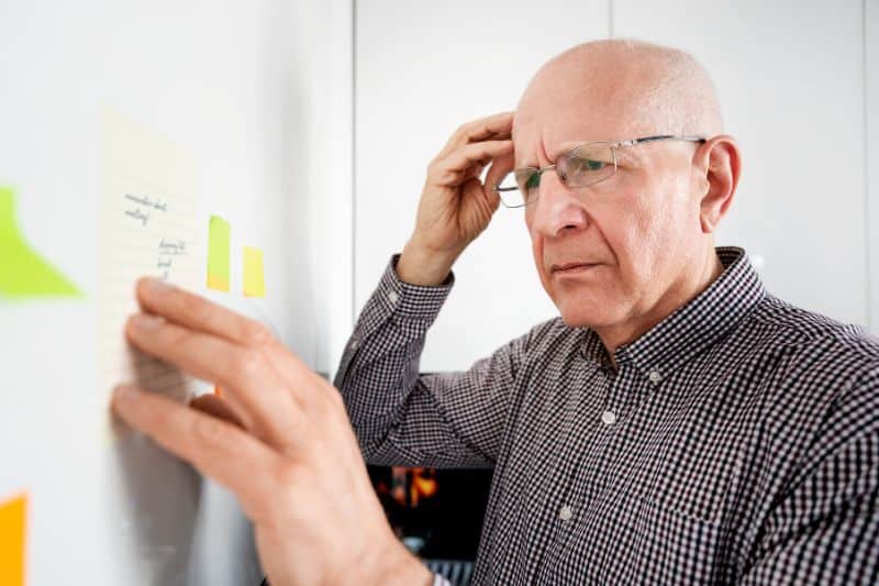 Elderly forgetful man with dementia and memory problem looking at notes.