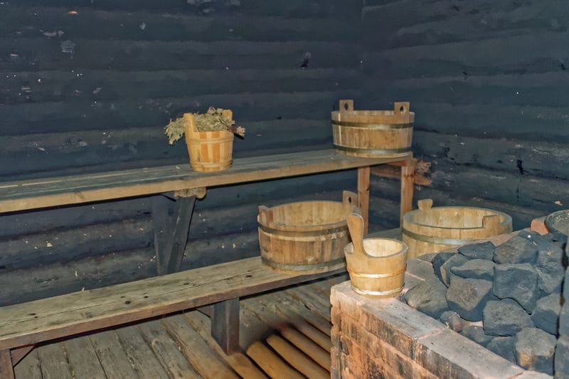 Inside a traditional Finnish smoke sauna with wooden benches, rustic sauna buckets, and birch branches, capturing the authentic essence of Finland's sauna culture.