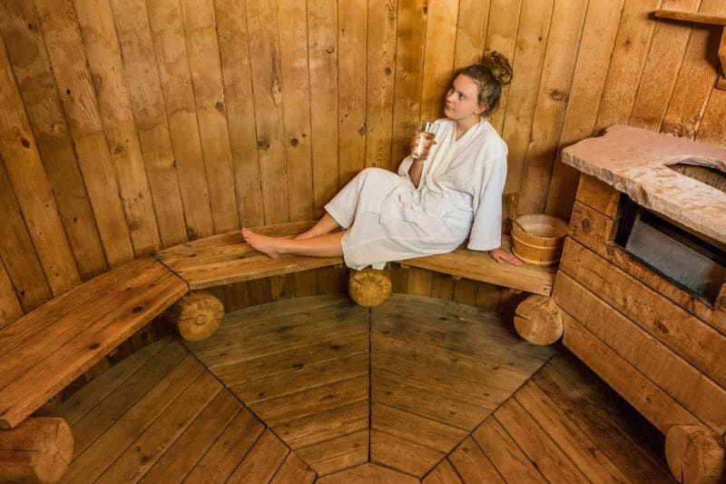 A woman relaxing inside a beautiful cedarwood sauna, stamping the fact that Cedar is the best wood for sauna.