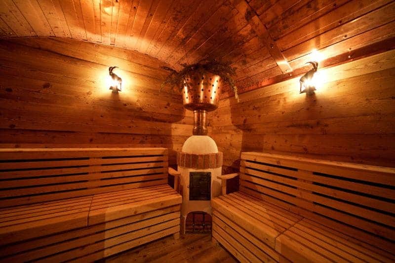 A cozy and rustic sauna with wooden benches, a wood-burning heater, and a copper pot hanging above, creating a warm and inviting atmosphere.