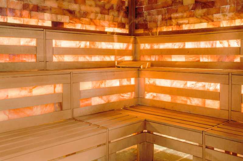Interior of a salt sauna with warm, glowing Himalayan salt bricks and wooden benches, highlighting the healing properties of salt saunas.