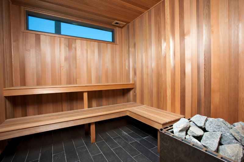 Interior view of a modern sauna room showcasing an electric sauna heater, wooden benches and a window, demonstrating an ideal setup for sauna enthusiasts.