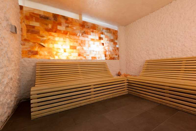 A salt sauna rest area with wooden lounge benches and a salt brick wall, ideal for unwinding and reaping health benefits.