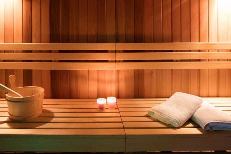 Cozy sauna setup with wooden bucket, ladle, and lit candles creating a serene atmosphere on the sauna benches.