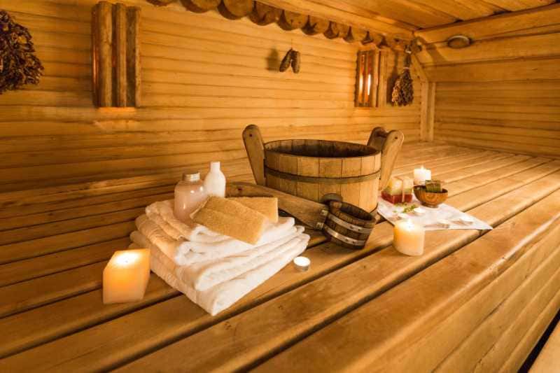 Cozy sauna interior featuring wooden walls and a bench, with towels, a wooden bucket, and candles, creating a serene and inviting atmosphere.