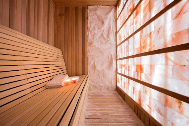 A serene salt sauna featuring a wooden bench and Himalayan salt wall, showcasing the relaxing environment that enhances wellness.