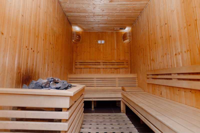 Spacious sauna room with a sauna heater, multiple wooden benches and a high ceiling, highlighting the design and capacity suitable for larger groups.