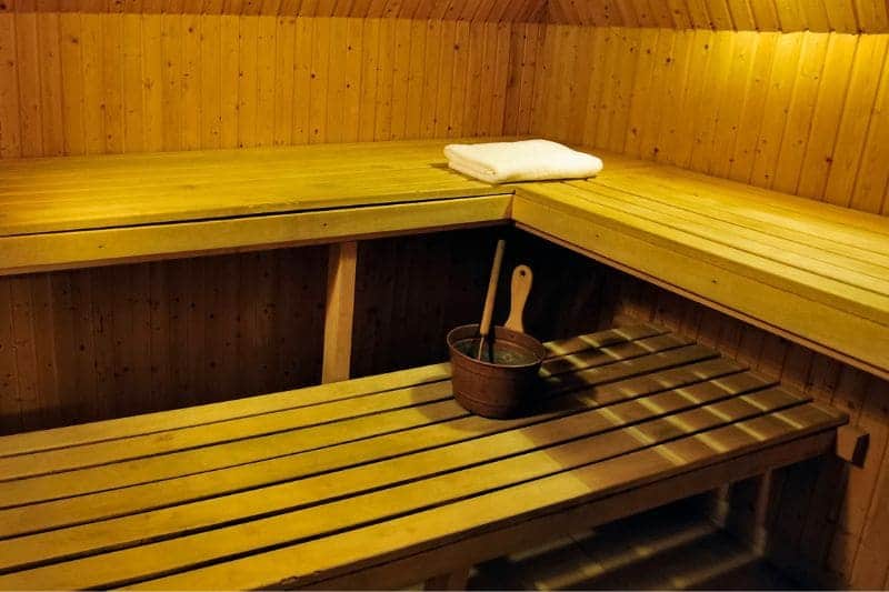A traditional wooden sauna with a bucket and ladle, and a neatly folded towel on the bench.