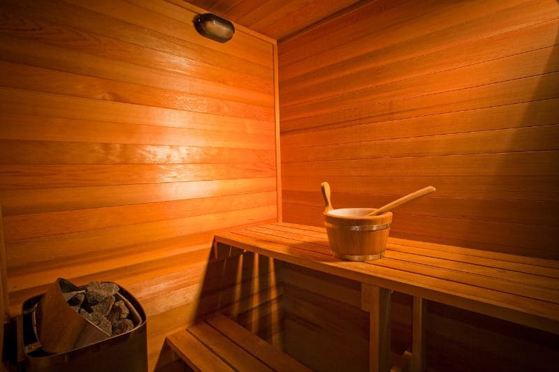 Traditional sauna with electric heater, featuring wooden benches and sauna bucket for a relaxing experience